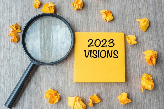 2023 visies woorden op gele notitie met verkruimeld papier en vergrootglas op houten tafel achtergrond nieuwjaar nieuwe start idee strategie en doelen concept