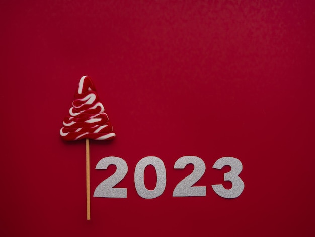 Foto 2023 e caramelle rosse bianche a forma di albero di natale su sfondo rosso
