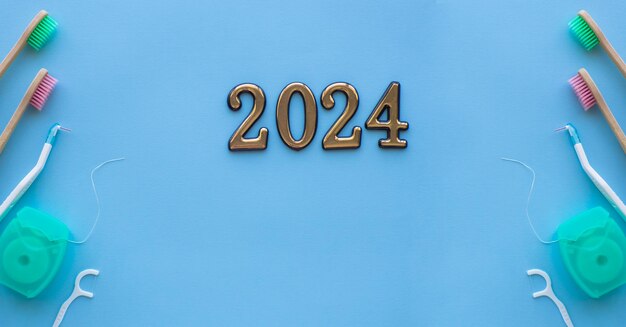 2024 and dental concept Close up view of photo with 2024 dental floss floss stick and wooden toothbrush on blue background with copy space Christmas medical card Merry Christmas and New Year