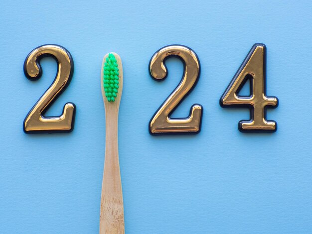 2024 and dental concept close up view photo with 2024 and wooden green toothbrush instead zero on blue background with copy space for text christmas medical card merry christmas and happy new year