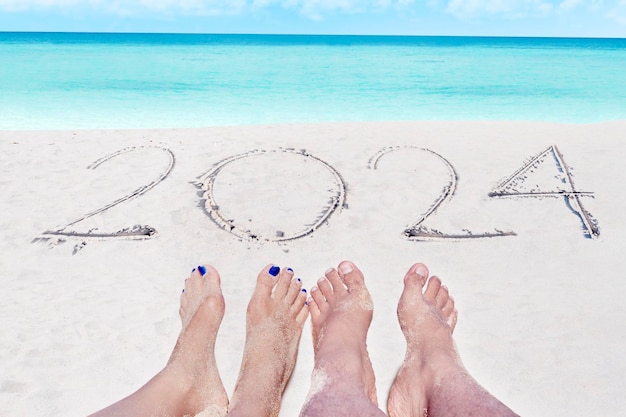 Концепция нового года 2024 Вид сверху на числа 2024 года, написанные на песке береговой линии с пенистыми волнами