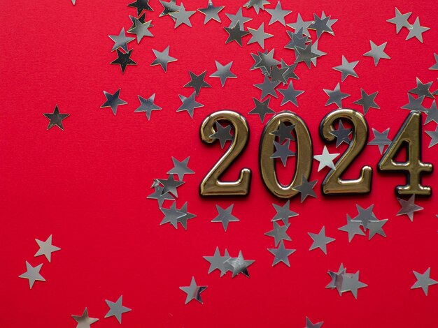 2024 op rode achtergrond met zilveren sterren en kopie ruimte Nieuwjaar plat lag concept van greating kaart Feestelijke kerstachtergrond Prettige Kerstdagen en Gelukkig Nieuwjaar Zilveren stervormige confetti