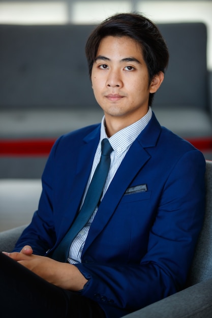 20s visionaire jonge knappe Aziatische uitvoerende zakenman draagt een formeel pak, zit met gekruiste benen comfortabel met ontspanning, kijkend naar de camera met vastberadenheid en vertrouwen in succes.