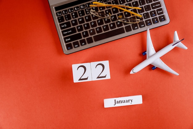 22 januari kalender met accessoires op zakelijke werkruimte bureau op computertoetsenbord, vliegtuig, glazen rode achtergrond