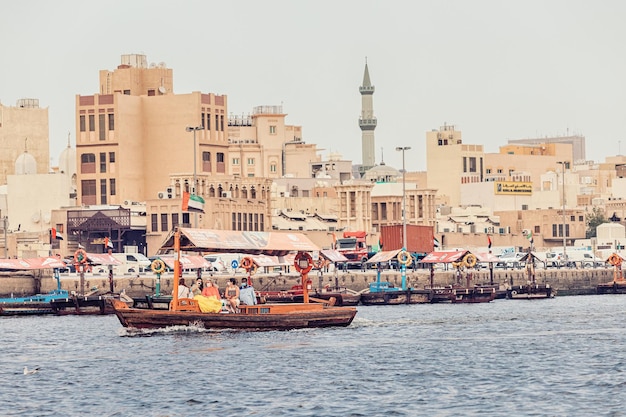 23 февраля 2021 года в Дубае (ОАЭ) деревянные лодки Abra Dhow перевозят пассажиров с одного берега Дубайского ручья на другой с минаретом мечети на заднем плане.