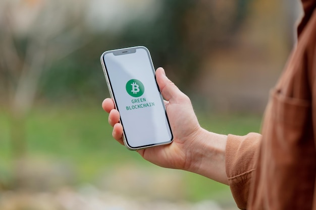 23 nov 2021 - Wroclaw, Poland: Man hold iPhone with green eco bitcoin logo and blockchain text. Trend of 2022 year