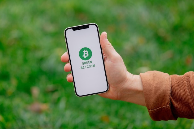 23 nov 2021 - Wroclaw, Polen: Man houdt iPhone vast met groen eco bitcoin-logo en blockchain-tekst. Trend van 2022 jaar