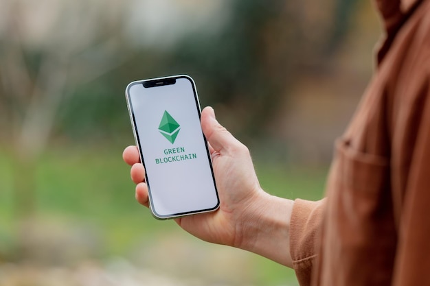 23 nov 2021 - Wroclaw, Polen: man houdt iPhone vast met groen eco ethereum-logo. Trend van 2022 jaar