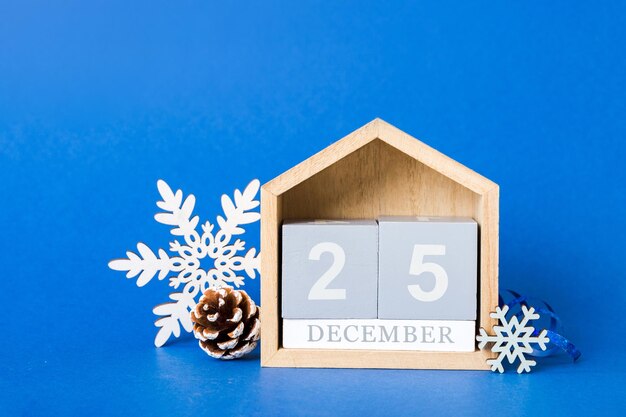 25 december Christmas composition on colored background with a wooden calendar with a gift box toys bauble copy space