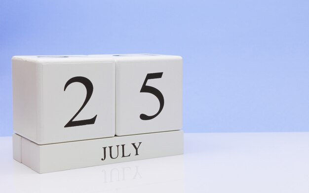 25 juli. Dag 25 van de maand, dagelijkse kalender op witte tafel met reflectie, met lichtblauwe achtergrond.