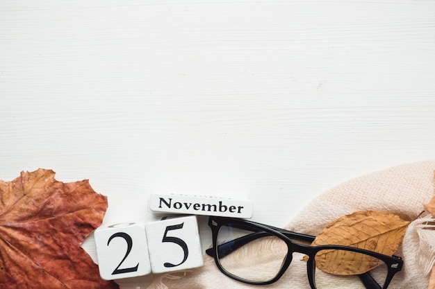 Foto 25 novembre nel calendario realizzato da cubi bianchi su una coperta con occhiali da vista e foglie. lay piatto