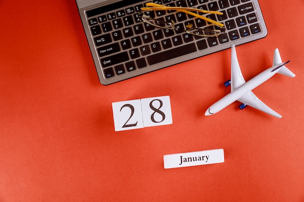 28 januari kalender met accessoires op zakelijke werkruimte bureau op computertoetsenbord, vliegtuig, glazen rode achtergrond