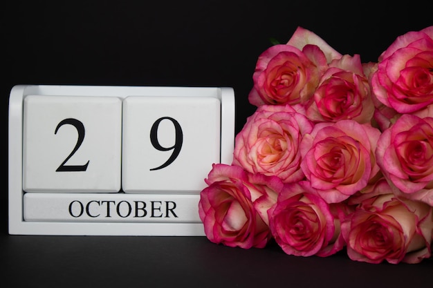 29 oktober houten kalender, wit op een zwarte achtergrond, roze rozen liggen in de buurt. Ansichtkaart met kopie