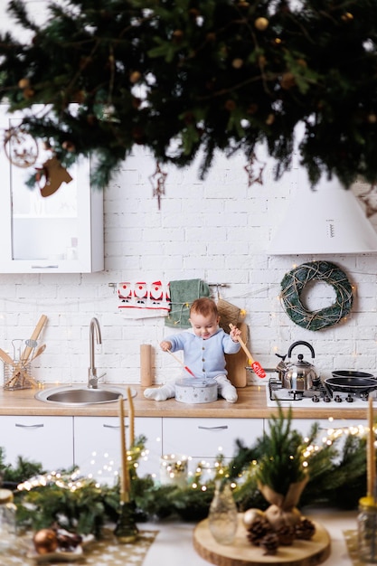 2-летний мальчик сидит на кухне, украшенной рождественскими украшениями.