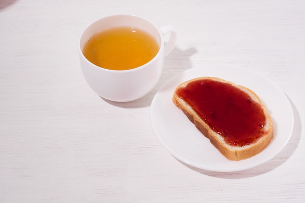 Ð¾pen sandwiche with homemade strawberry jam and cup of tea on a white wooden surface