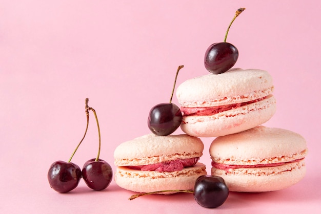 사진 분홍색 표면에 분홍색 크림을 곁들인 체리가 들어간 베이지 색 프랑스 마카롱 3 개, 쿠키