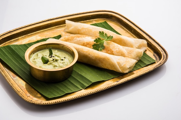 3 dosa rolls with coconut chutney in a brass tray over coconut leaf, favourite south indian meal