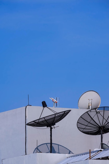 3 satellite dishes with tv antenna on top of the old gray building against blue clear sky