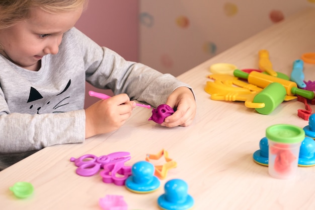 3歳の女の子のクリエイティブアート。カラフルな粘土の粘土で遊ぶ子供の手。自己隔離covid-19、オンライン教育、ホームスクーリング。家で勉強している幼児の女の子、家の学習。