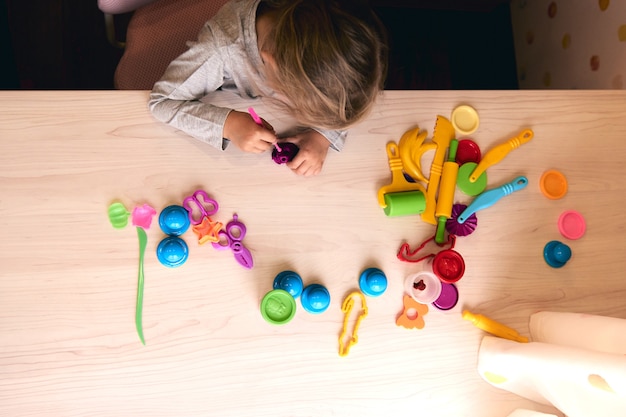 3歳の女の子のクリエイティブアート。カラフルな粘土の粘土で遊ぶ子供の手。自己隔離Covid-19、オンライン教育、ホームスクーリング。家で勉強している幼児の女の子、家の学習