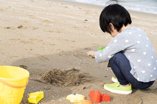 3歳のアジアの子供はビーチで砂を再生します。