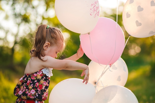 3 years old gil is playing with white and pink balloons in the summer garden