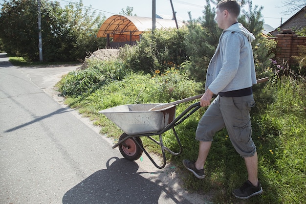 A 30-year-old caucasian man carries a garden wheelbarrow for loading sand to fill the paths with concrete at his summer cottage