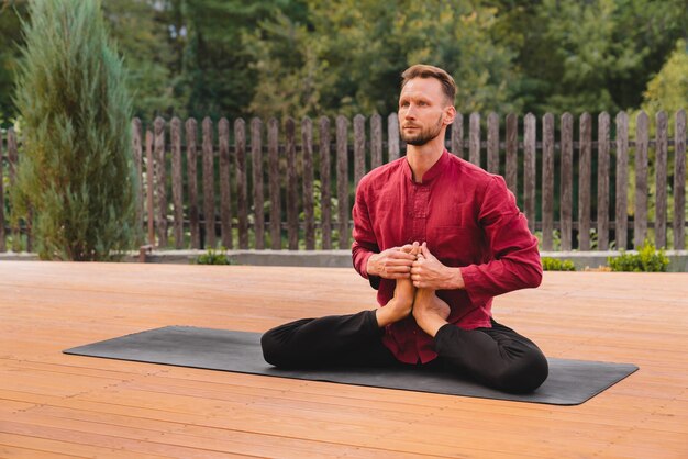 30s male yogi sitting in lotus holding his feet together on mat
in the garden