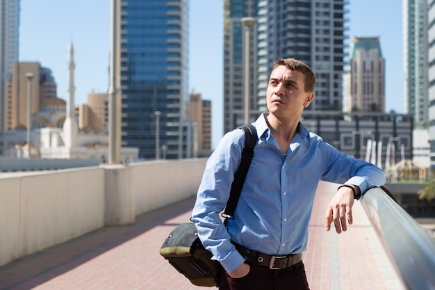 A 35 40-year-old man stands in center of a big city and looks around with interest.