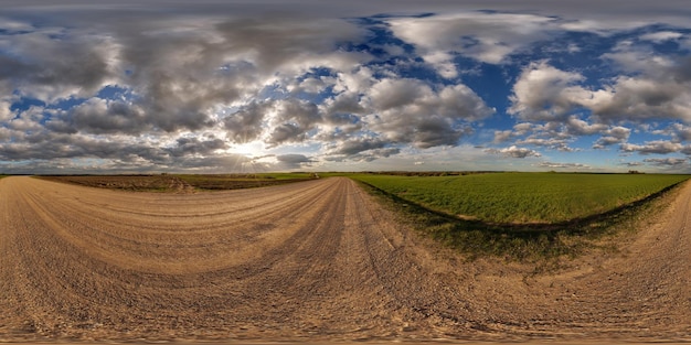 360° панорамный вид на бездорожной гравийной дороге среди полей в весенний день с красивыми облаками в равноугольной полной бесшовной сферической проекции, готовой для VR AR