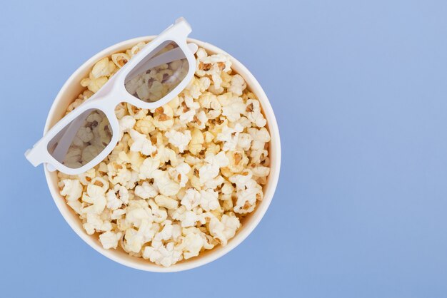 I vetri 3d si trovano su una tazza con popcorn isolato su una priorità bassa blu pastello. concetto di cinema. disteso.