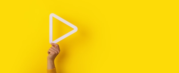 Foto pulsante di riproduzione multimediale 3d in mano su sfondo giallo, layout panoramico