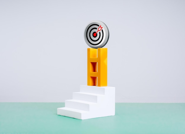 3d moderne doel dartboard bullseye icoon op de top van gele ladder op trap stappen op groene tafel witte achtergrond Business markt groei marketing doel inspanningen naar doelen leider visie concept