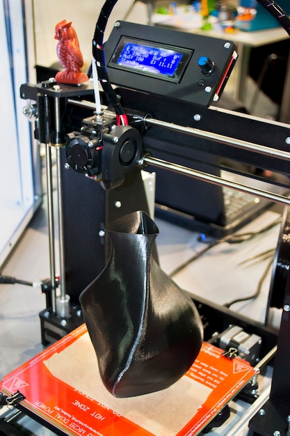 3D-принтер, распечатывающий модель в виде черной вазы крупным планом. Понятие современной аддитивной технологии. 4-я промышленная революция.