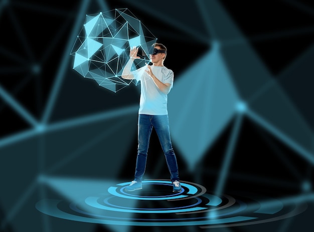 3D-technologie, augmented reality, gaming, cyberspace en mensenconcept - gelukkige jonge man met virtual reality-headset of 3D-bril die een spel speelt en een hologram met een lage polyvorm aanraakt