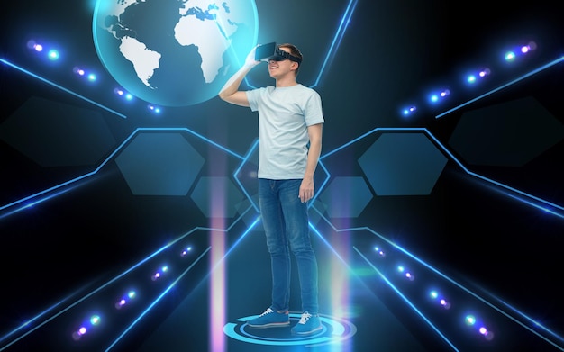 3D-technologie, virtual reality, cyberspace, wereldwijde communicatie en mensenconcept - jonge man met virtual reality-headset of 3D-bril kijkend naar aardehologram over zwarte achtergrond en lichten