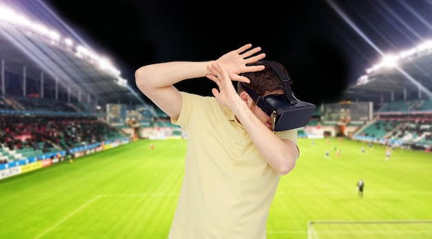 3D-technologie, virtual reality, sport, entertainment en mensenconcept - gelukkige jonge man met virtual reality-headset of 3D-bril die spel speelt over voetbalveld op stadionachtergrond