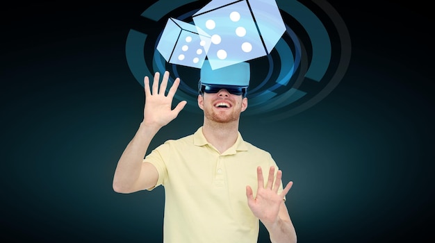 Фото 3d-технологии, виртуальная реальность, киберпространство, развлечения и концепция людей - счастливый молодой человек с гарнитурой виртуальной реальности или 3d-очками, играющий в игру с проекцией костей казино на черном фоне