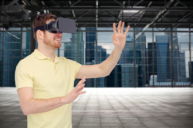 Photo 3d technology, virtual reality, entertainment and people concept - happy young man with virtual reality headset or 3d glasses playing game over industrial empty room and city panorama background