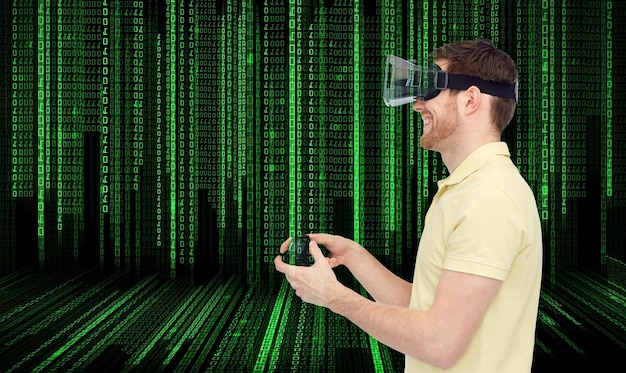 3d technology, virtual reality, entertainment and people concept - happy young man with virtual reality headset or 3d glasses playing with game controller gamepad over binary code background