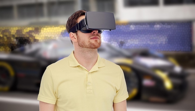 3d technology, virtual reality, entertainment and people concept - young man with virtual reality headset or 3d glasses playing car racing game over street race background