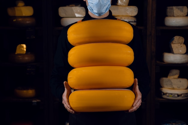 4 큰 노란색 치즈 바퀴 손에. 코로나 바이러스 COVID-19에 대한 보호를 위해 마스크 판매자. 둥근 치즈를 들고.