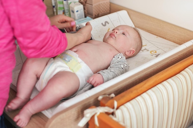 Foto 4 maanden oude babyjongen, aan de commode, zijn moeder die kleren aantrekt