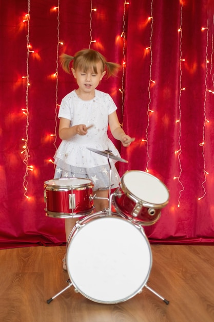 Photo 4 year old girl plays on drums on red  with garlands