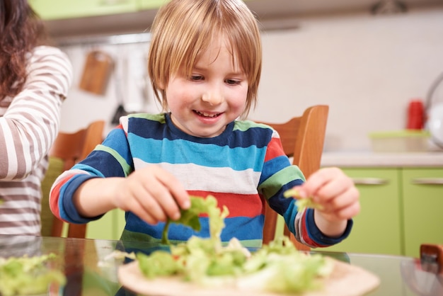 4-летний дошкольник готовит салат из свежих овощей на кухне дома