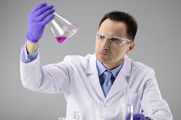 40s Male doctor or Chemist researcher closely analyzing red liquid in flask