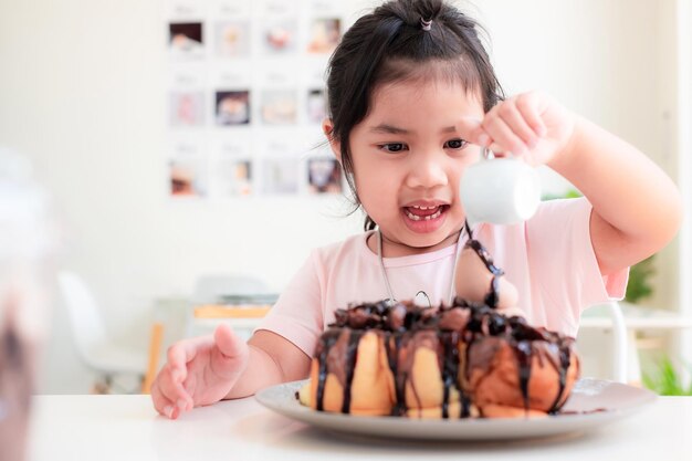 45 jaar oud schattig Aziatisch meisje glimlacht en giet chocolade op chocolade toast op de witte tafel in een koffiehuisHoney Toast is een zoet dessert waar kinderen van houden Ontspan gelukkig familie tijd concept