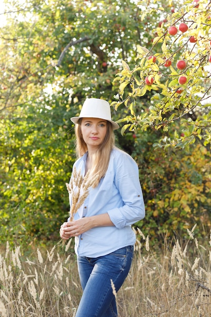 45 year old woman in a blue shirt and hat posing in an apple orchard