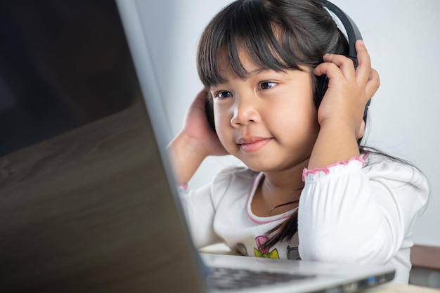 45 years old asian girl wearing white shirt is studying online\
via computer using bluetooth headphones at home distance education\
concept