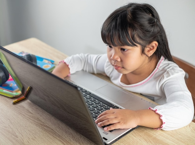 45 years old Asian girl wearing white shirt is studying online via computer using bluetooth headphones at home distance education concept